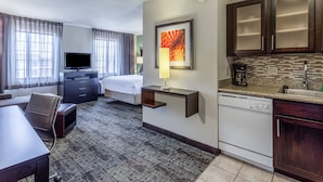 A hotel room with a bed, a desk, a television, a coffee maker, and a kitchen area with a dishwasher. - Staybridge Suites Davenport by IHG (Davenport)