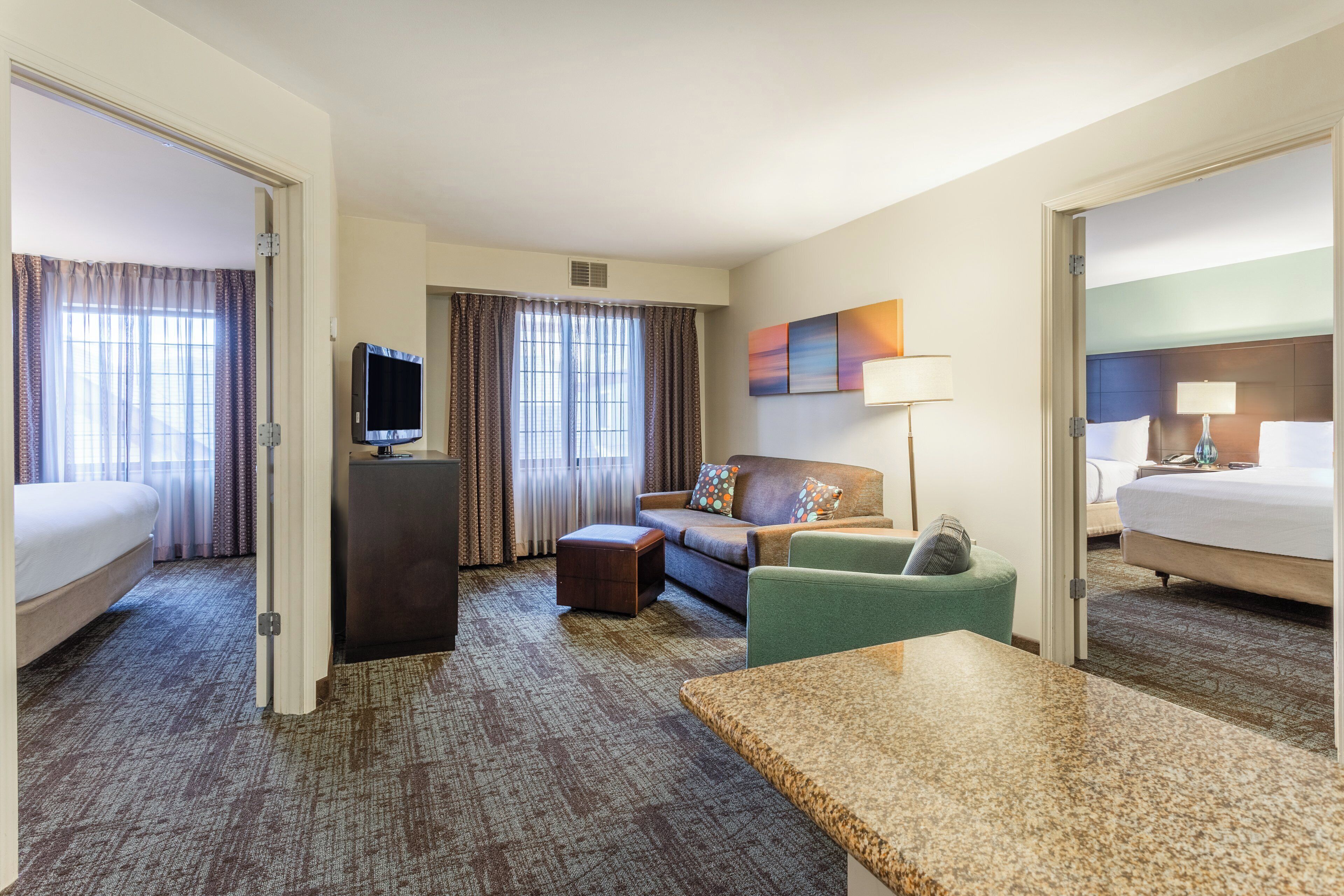 A hotel room with a bed, a sofa, a desk, a television, and a window with curtains.