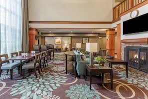 A hotel lobby with a dining area, seating arrangements, a fireplace, and artwork on the walls. - Staybridge Suites Davenport by IHG (Davenport)