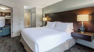 A hotel room with a large bed, a bedside table with a lamp, a nightstand, a wardrobe, and a bathroom with a shower curtain.