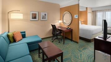 A hotel room with a blue sofa, a desk with a lamp, a bed, a TV, and a large mirror.