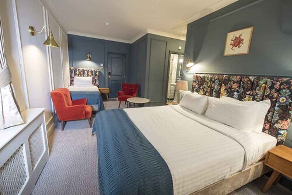 A hotel room with a large bed, a desk, a chair, and a small table.