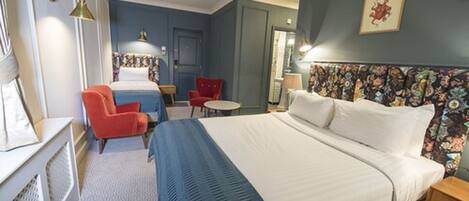 A hotel room with a large bed, a desk, a chair, and a small table.