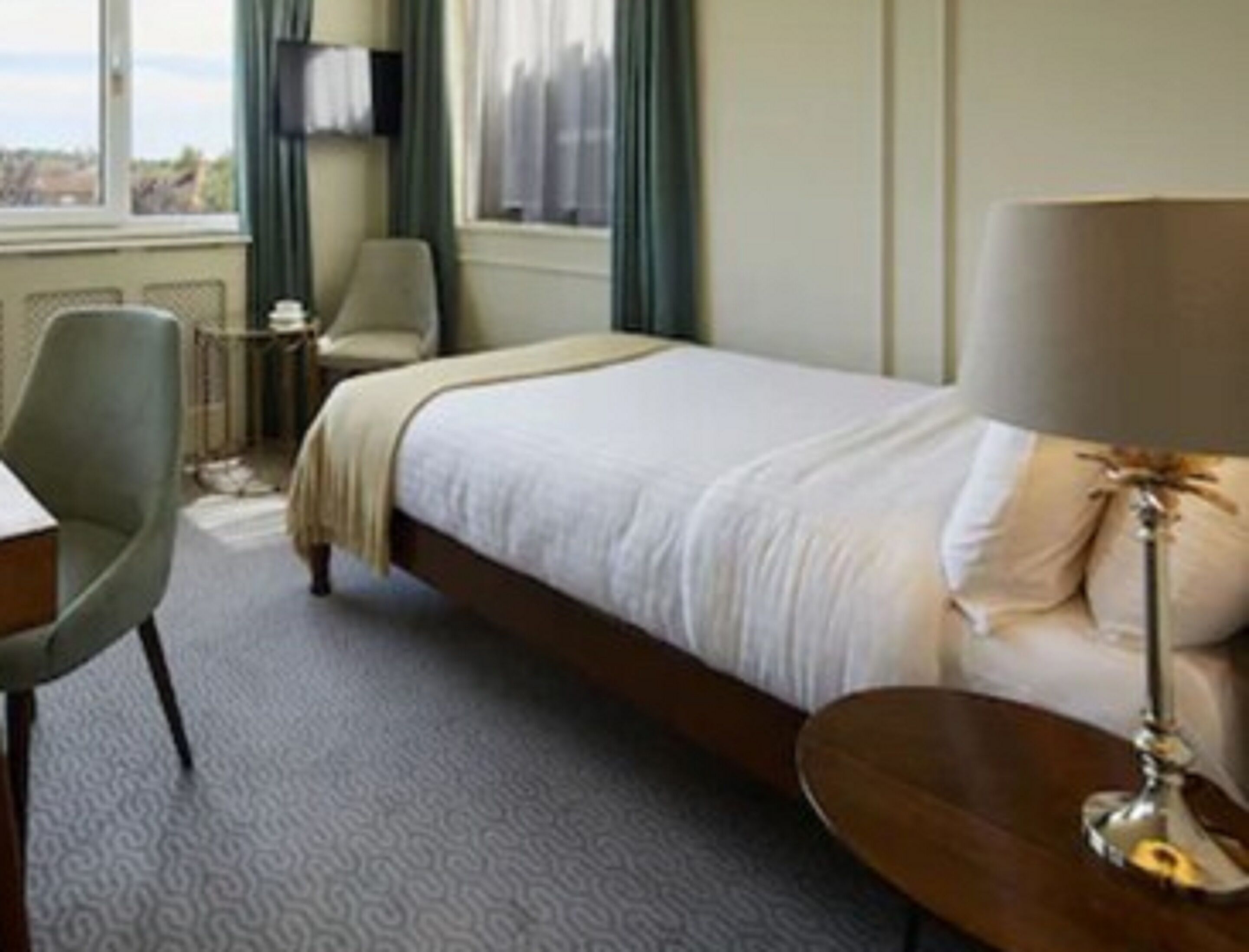 A hotel room with a bed, a chair, a small table, and a lamp.