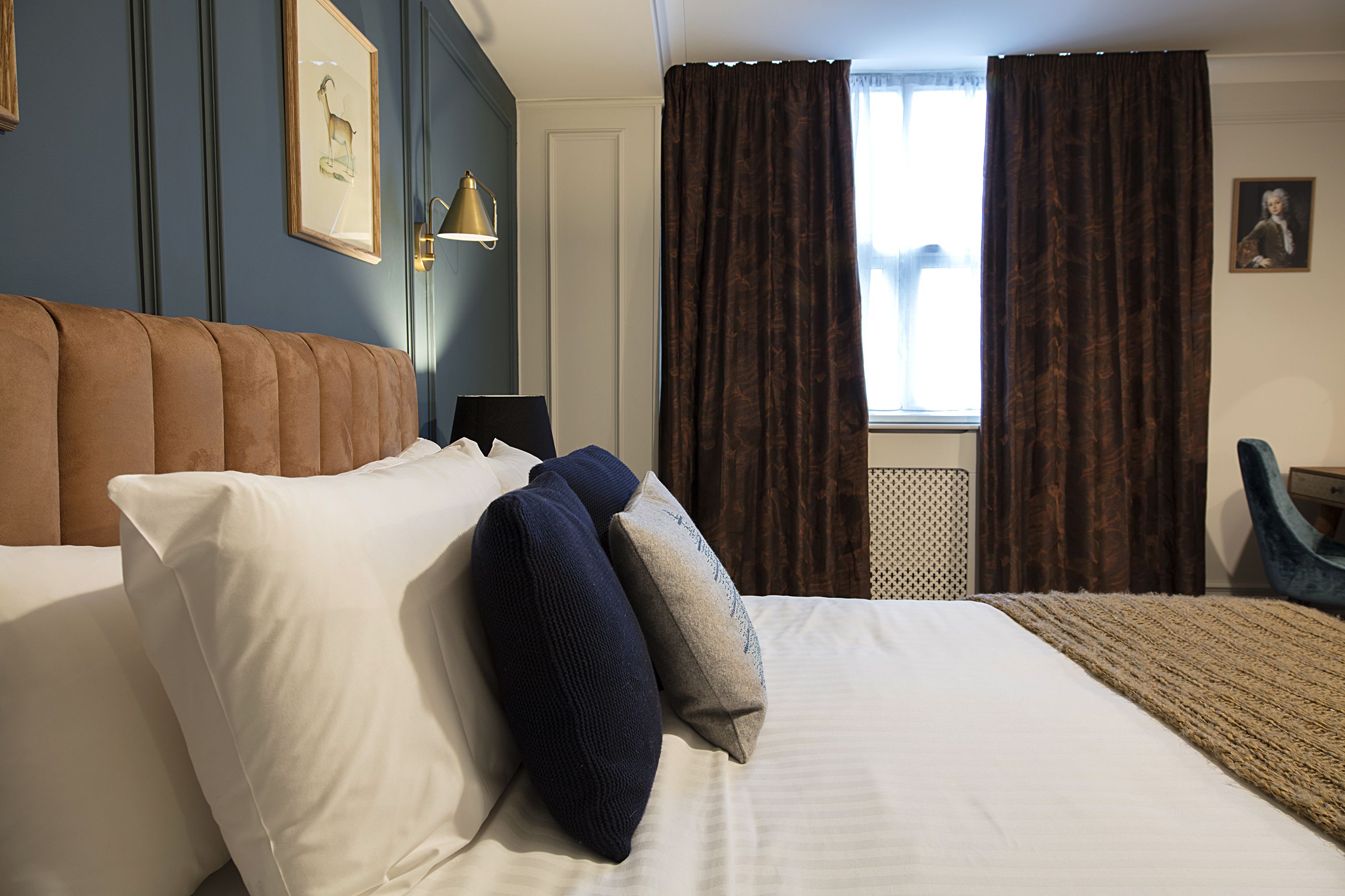A hotel room with a large bed, a headboard, a nightstand, a lamp, a window with curtains, and a framed picture on the wall.