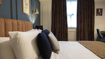 A hotel room with a large bed, a headboard, a nightstand, a lamp, a window with curtains, and a framed picture on the wall.