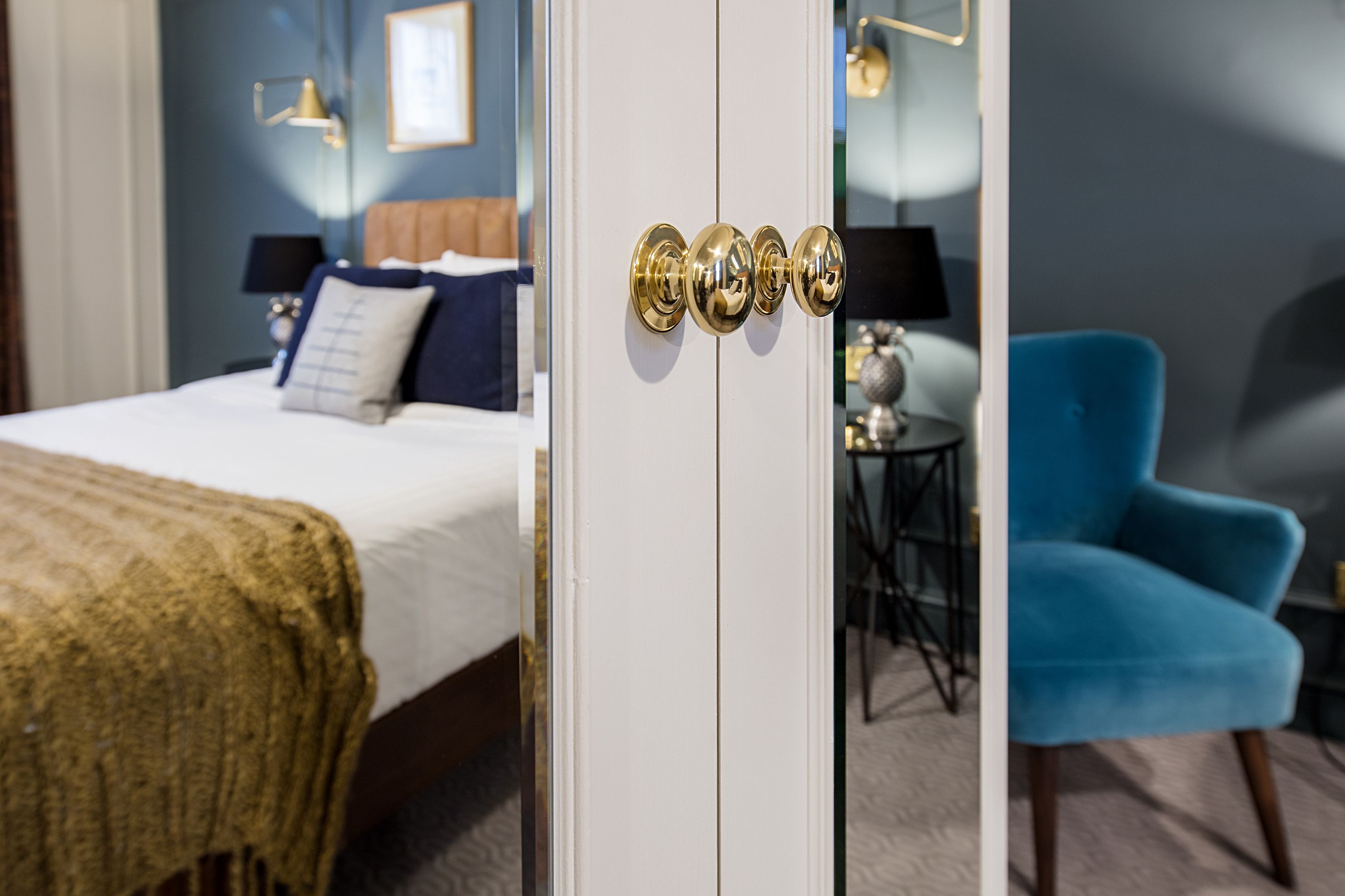 A hotel room with a bed, a blue armchair, and a door with four golden handles.