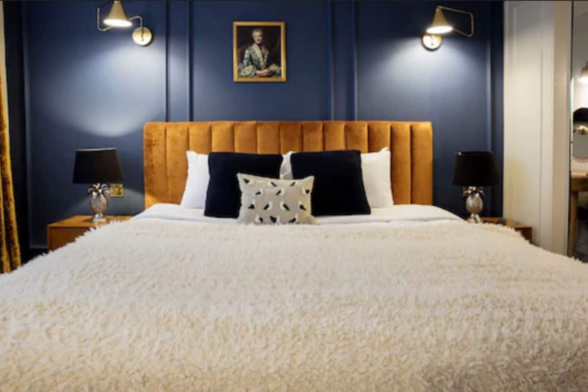 A bedroom with a large bed, two bedside tables with lamps, a framed picture on the wall, and a blue accent wall.