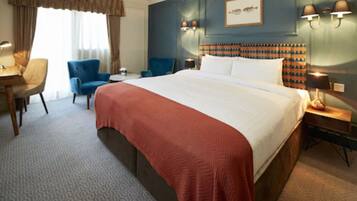 Quarto de hotel com uma cama grande, uma mesa, duas cadeiras e uma mesinha de cabeceira com luminárias.