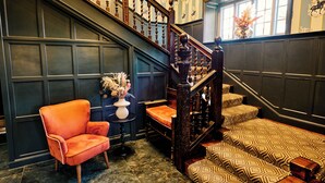 A grand staircase with ornate woodwork, a plush orange armchair, patterned cushions, and a vase of flowers. - Cromwell Hotel Stevenage (Stevenage)