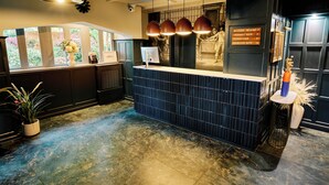 A reception area with a blue tiled counter, a computer monitor, and a sign indicating directions to the Brasserie, Lounge & Bar, and Boucherie Suite. - Cromwell Hotel Stevenage (Stevenage)