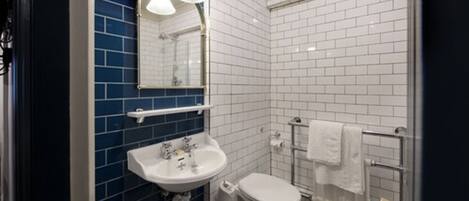A bathroom with a white sink, a white toilet, and a blue-tiled shower area.
