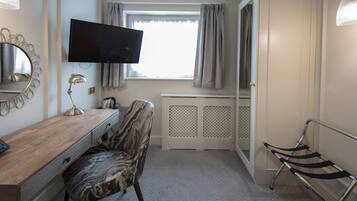Un dormitorio con un escritorio de madera, una silla, un televisor, un radiador y una ventana con cortinas.