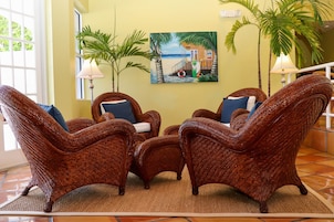 Una habitación con sillones de mimbre, un cuadro de una playa y una planta grande en maceta.