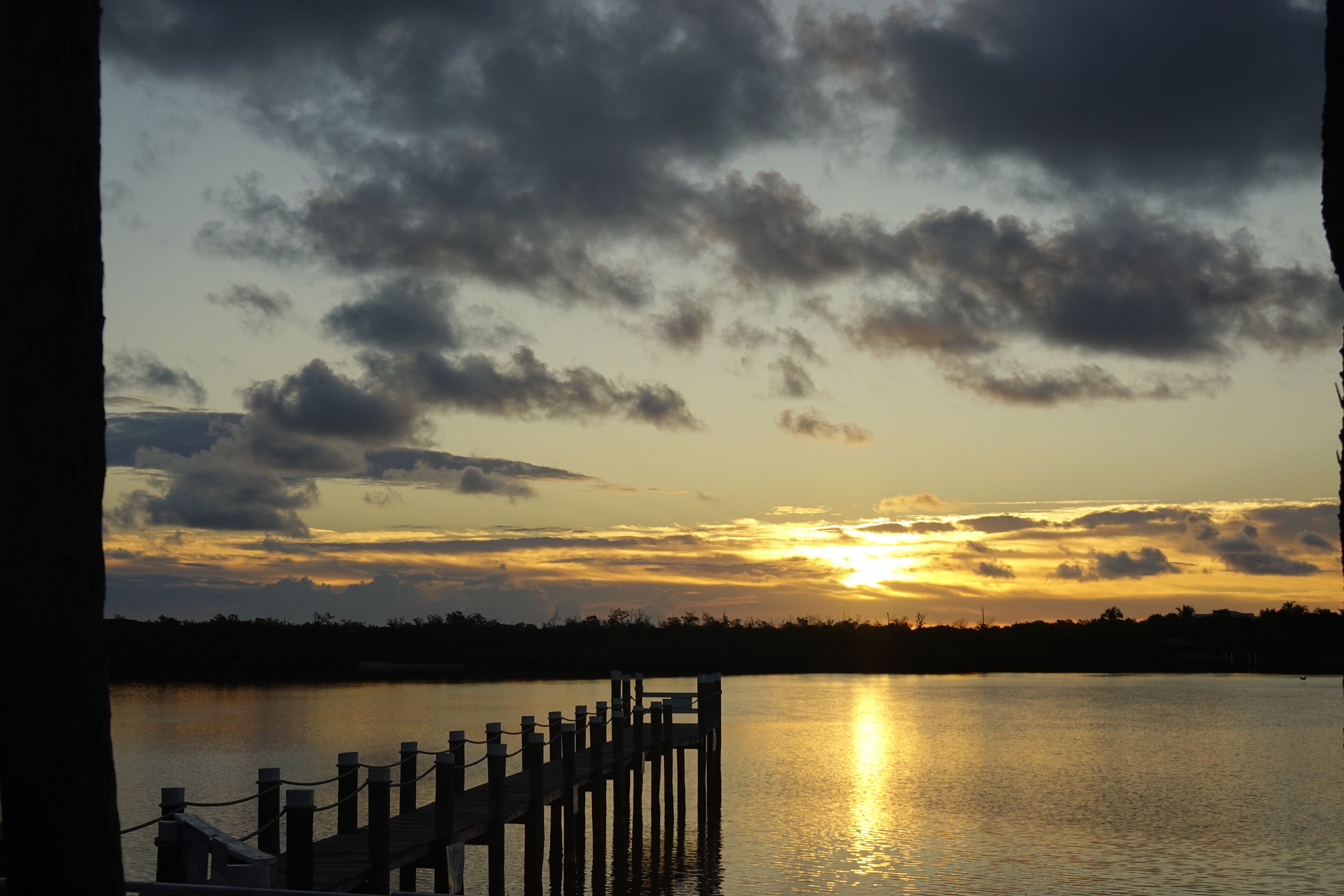A sunset over a calm lake with a wooden dock extending into the water.