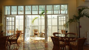 A spacious indoor area with a large glass door leading to an outdoor patio. Inside, there are wicker chairs and a round table, with potted plants and a ceiling fan visible. - Jupiter Waterfront Inn (Jupiter)
