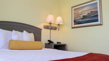 Una cama bien hecha con ropa de cama blanca y roja, una mesita de noche con una lámpara, un teléfono y una fotografía enmarcada de barcos en la pared.