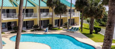 A hotel with a pool, palm trees, and a turquoise roof.