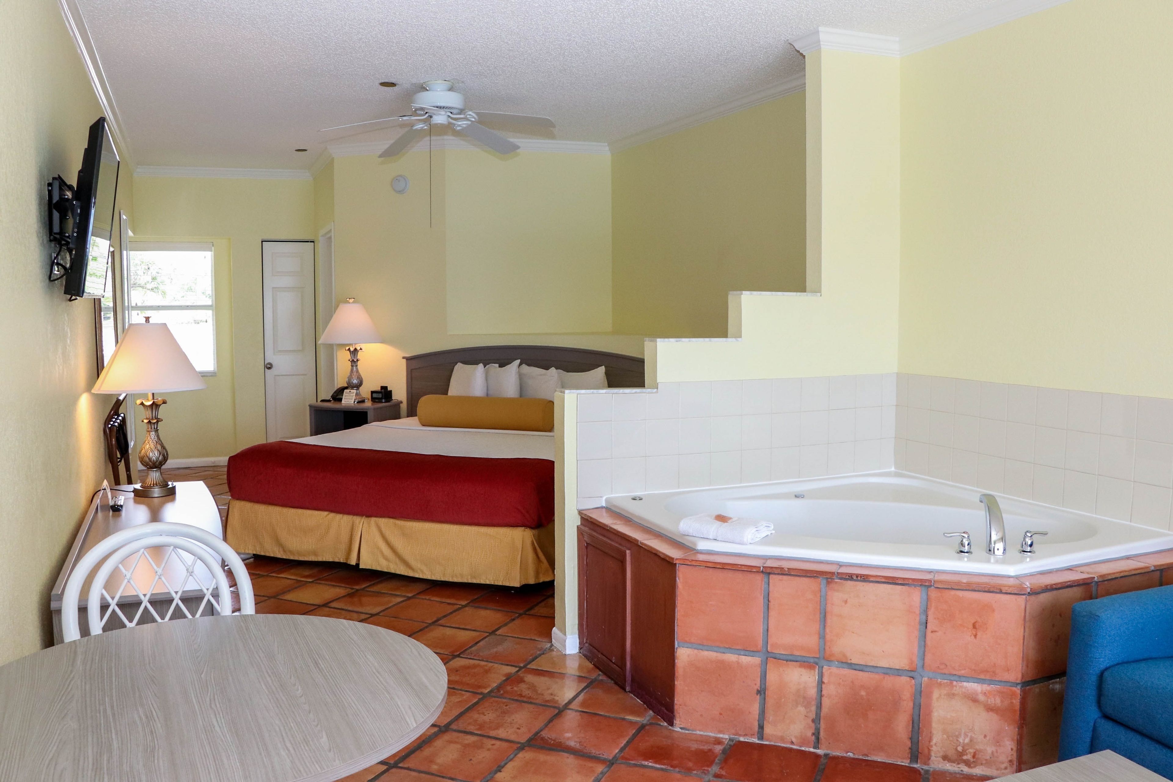 Una habitación de hotel con cama, zona de estar con mesa y sillas, bañera y ventilador de techo.