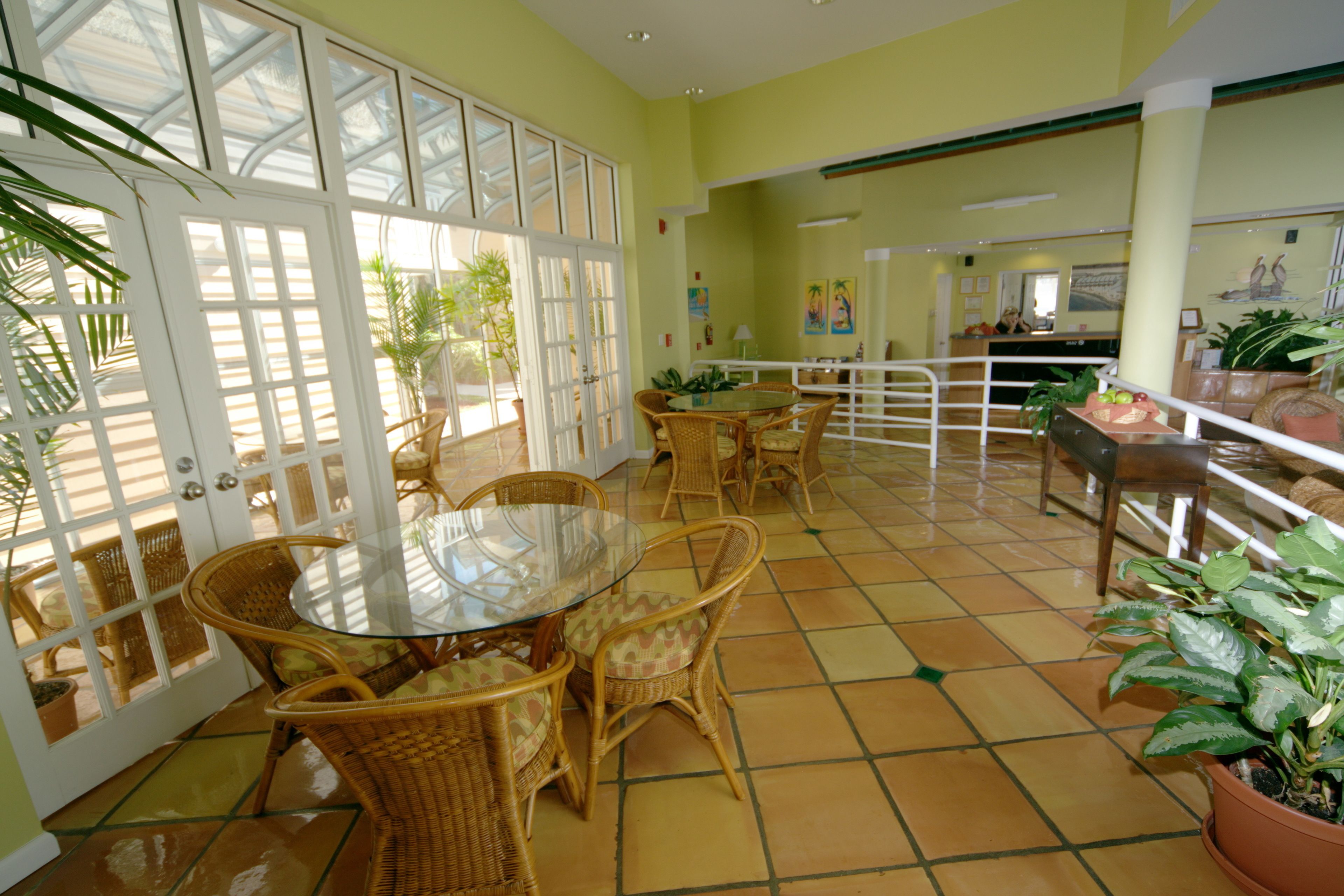 A sunlit patio with wicker furniture, a glass table, and potted plants.