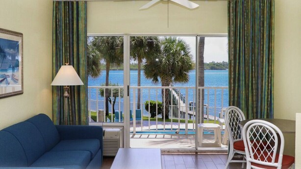 A room with a blue sofa, a table, and chairs, a ceiling fan, and a view of the sea through large windows. - Jupiter Waterfront Inn (Jupiter)