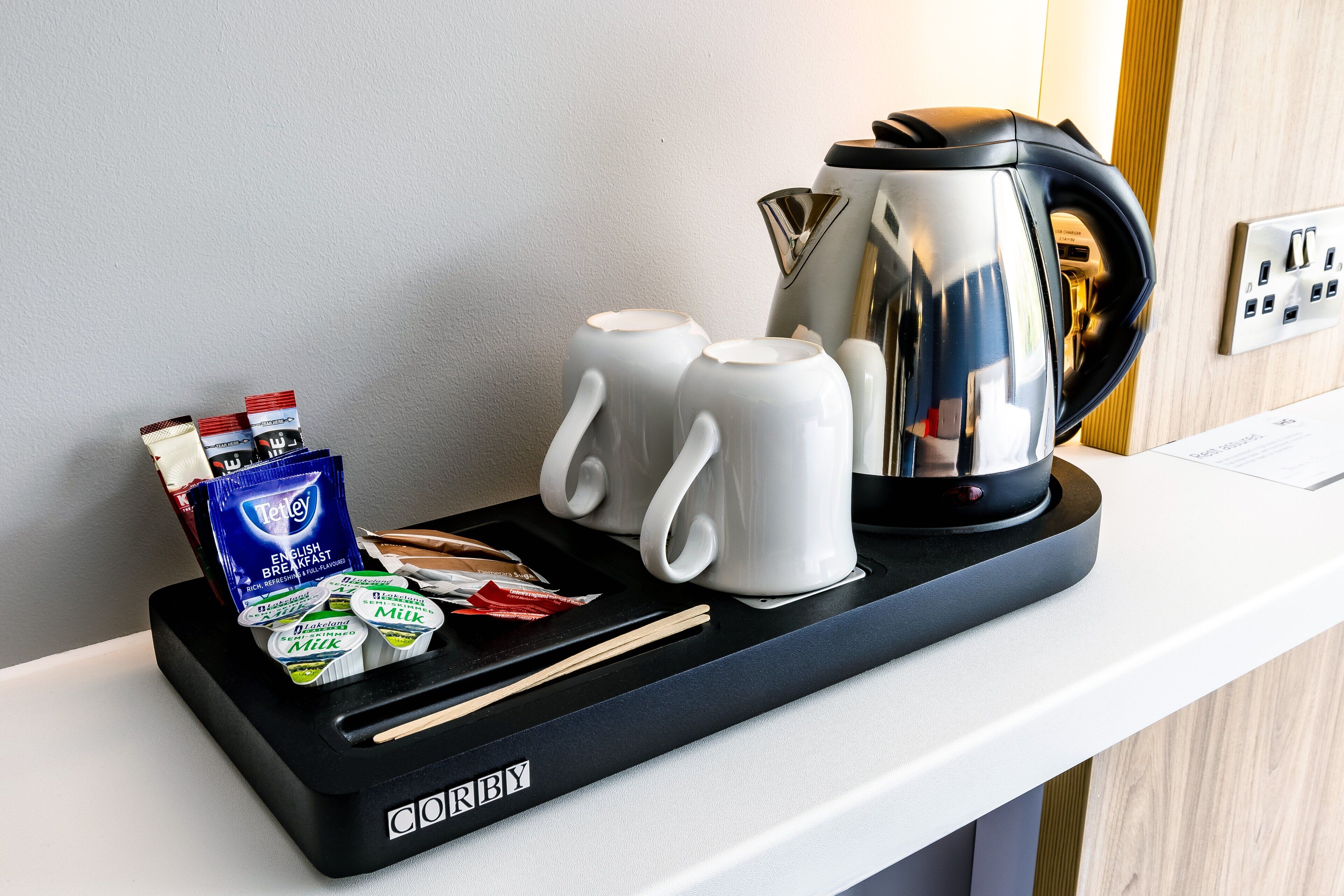 A hotel room's breakfast trolley with a coffee maker, two white mugs, a tray with breakfast items, and a box of tea.