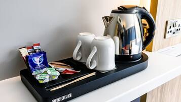 A hotel room's breakfast trolley with a coffee maker, two white mugs, a tray with breakfast items, and a box of tea.