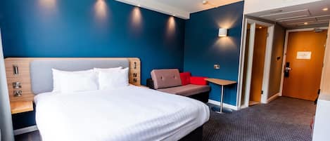A hotel room with a large bed, a seating area with a red chair, and a small table.