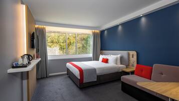 Una habitación de hotel moderna con una cama grande, un sofá, una mesita y una ventana con cortinas.