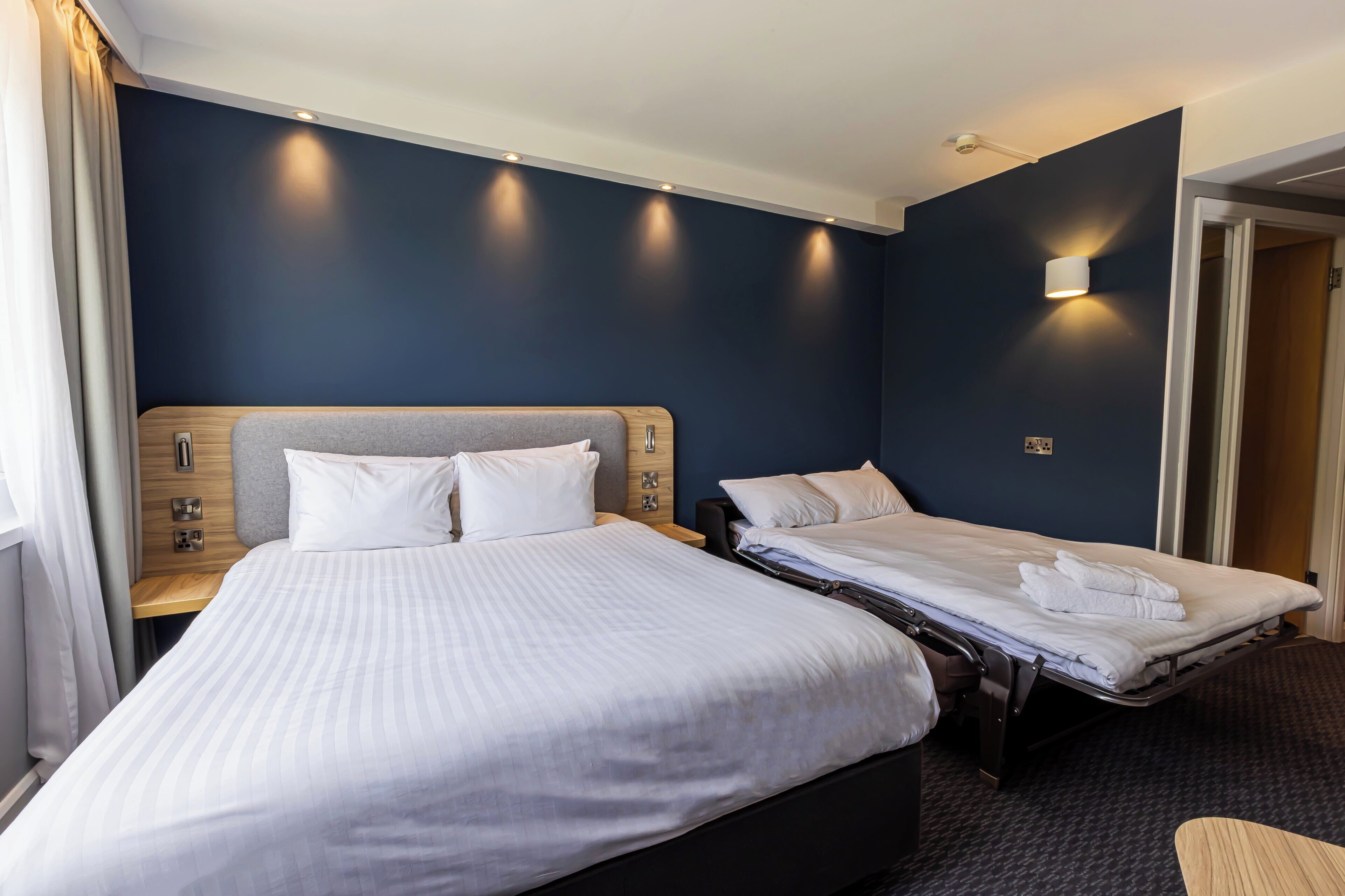 Een hotelkamer met twee bedden, een houten hoofdbord, een nachtkastje met een lamp en een wandlamp.