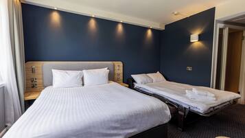 A hotel room with two beds, a wooden headboard, a bedside table with a lamp, and a wall-mounted light fixture.