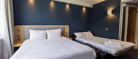A hotel room with two beds, a wooden headboard, a bedside table with a lamp, and a wall-mounted light fixture.