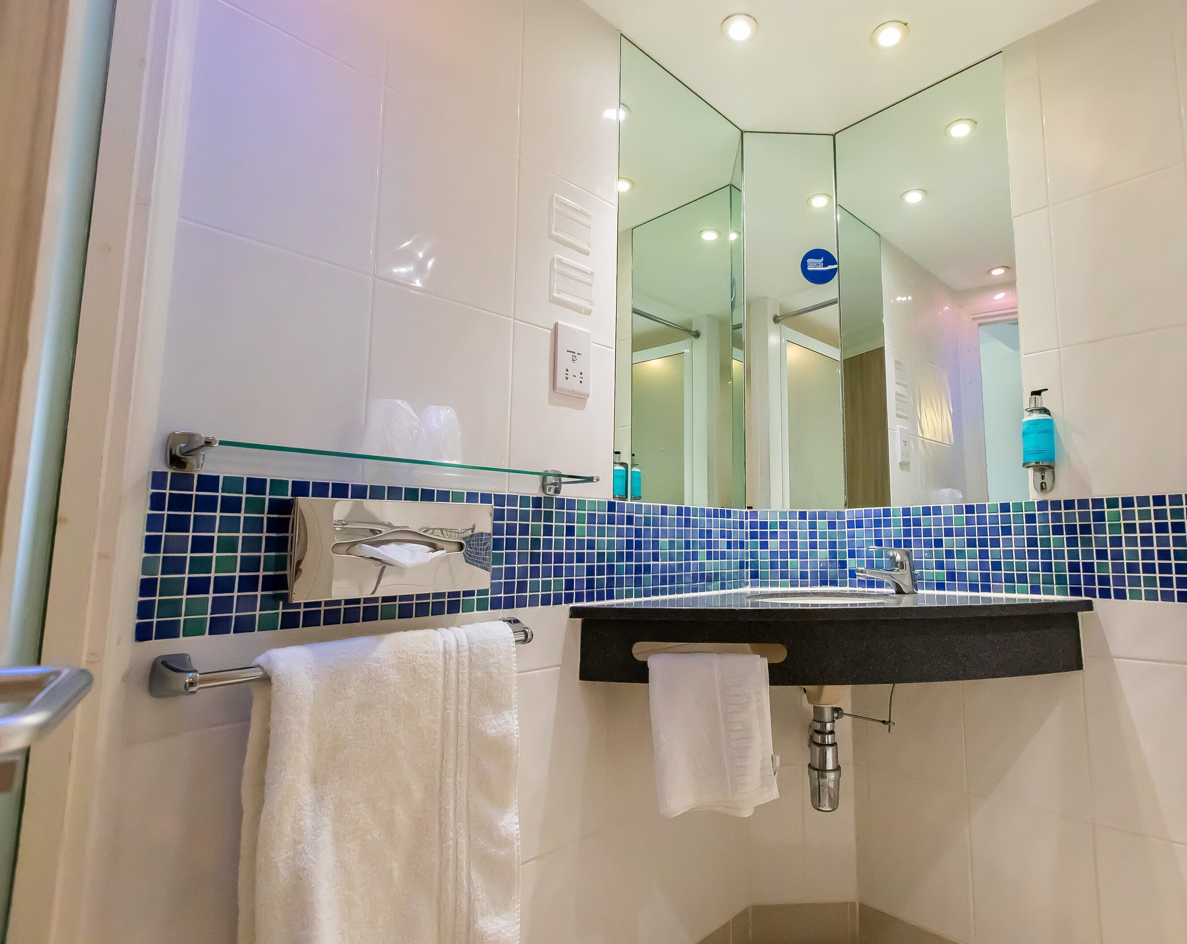 Un baño con cabina de ducha de vidrio, un lavabo con espejo y un perchero con una toalla blanca.