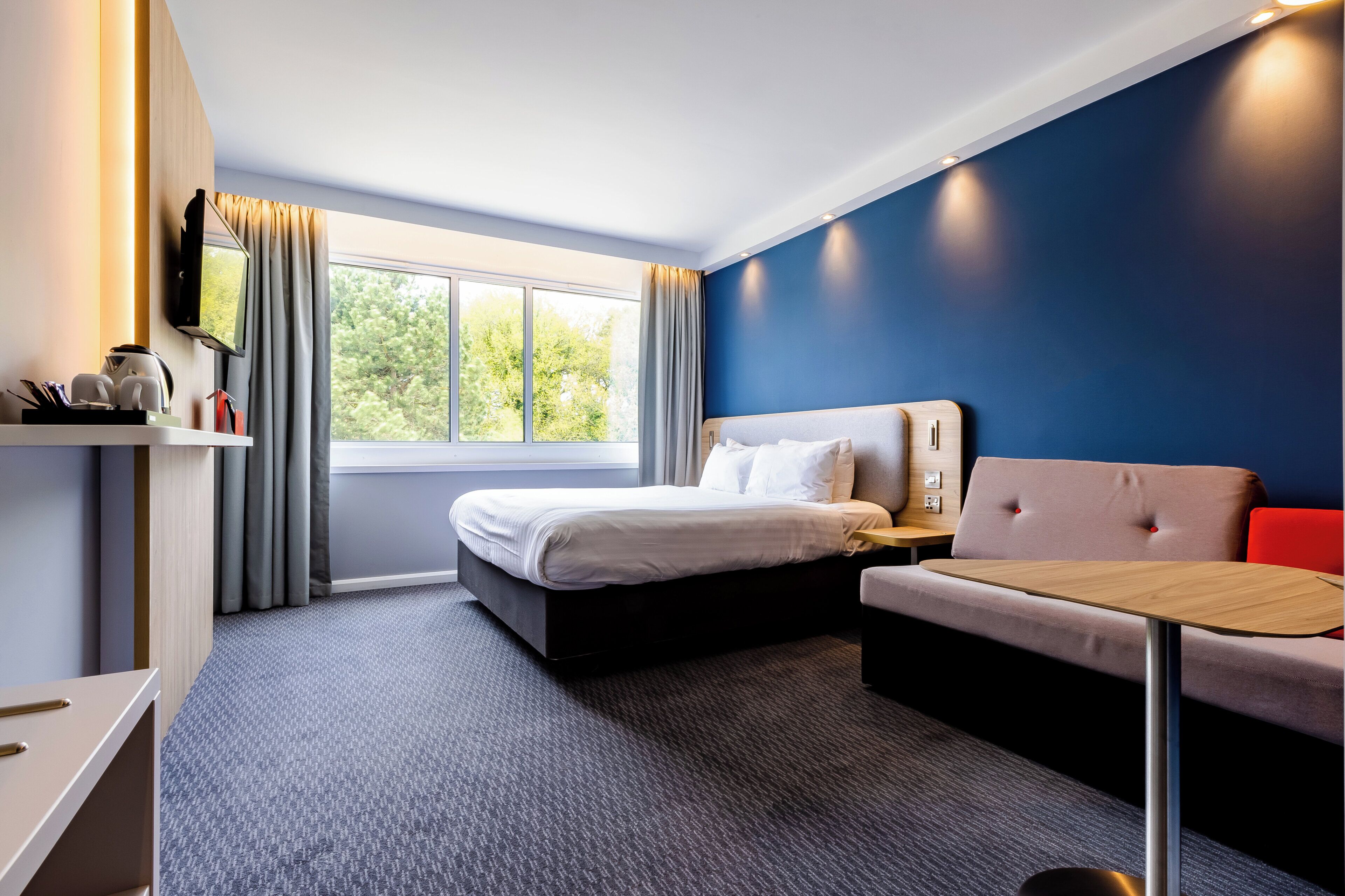 A hotel room with a bed, a desk, a chair, and a sofa.
