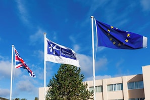 Three flags on flagpoles, including the UK flag, a hotel flag, and the EU flag.