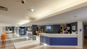 A modern hotel lobby with a reception desk, seating area, and a vending machine. - Holiday Inn Express Norwich by IHG (Norwich)