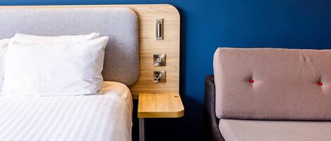 Una habitación de hotel con una cama, una mesita de noche, una silla y un enchufe en la pared.