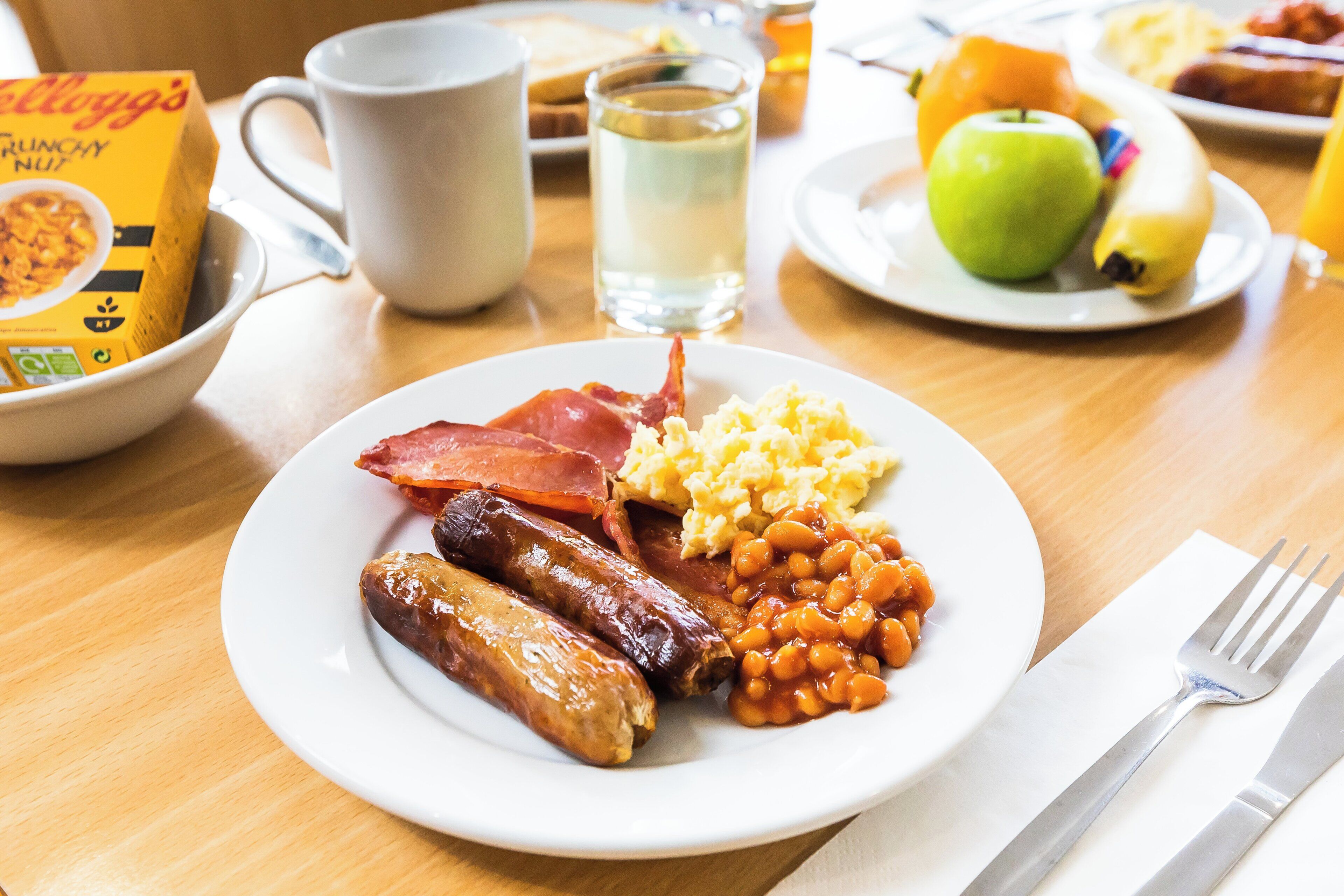 A breakfast plate with sausages, bacon, beans, and scrambled eggs.