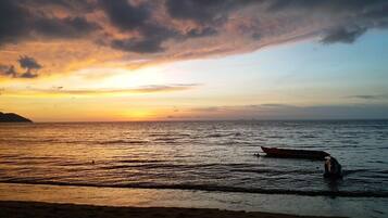 A beach scene with a boat on the water and a distant landmass.