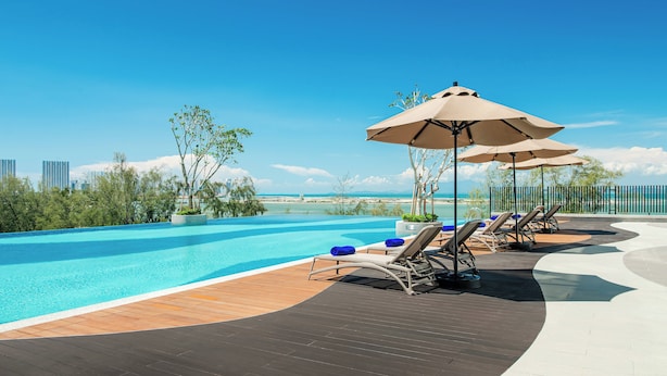 A poolside area with lounge chairs and umbrellas, overlooking a clear blue sky and a distant coastline. - Ascott Gurney Penang (George Town)