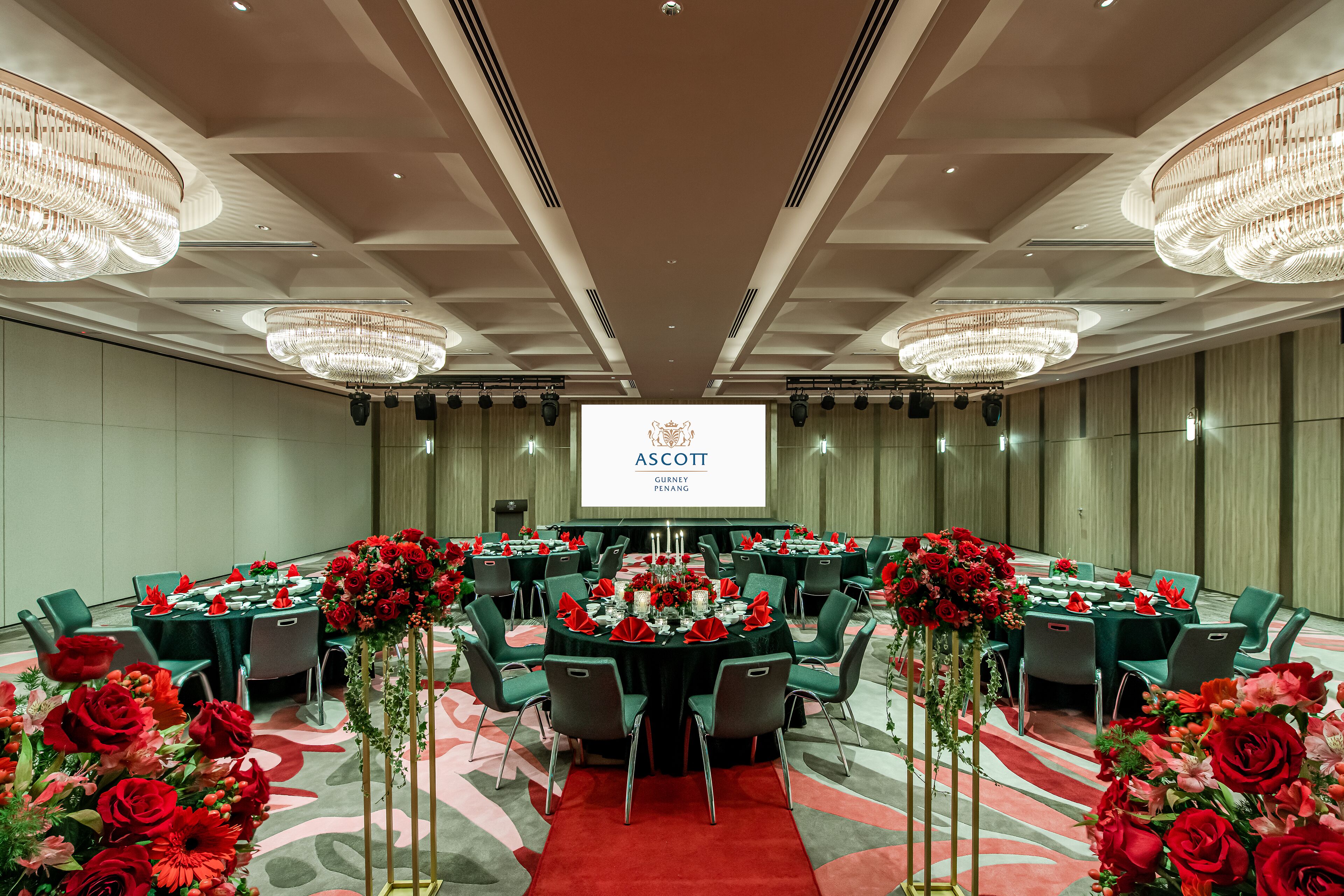 A conference room with round tables, green chairs, and red floral centerpieces.