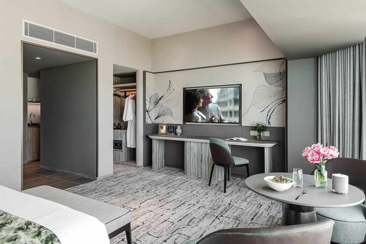 Habitación de hotel moderna con zona de comedor, televisor montado en la pared y vistas a la ciudad.