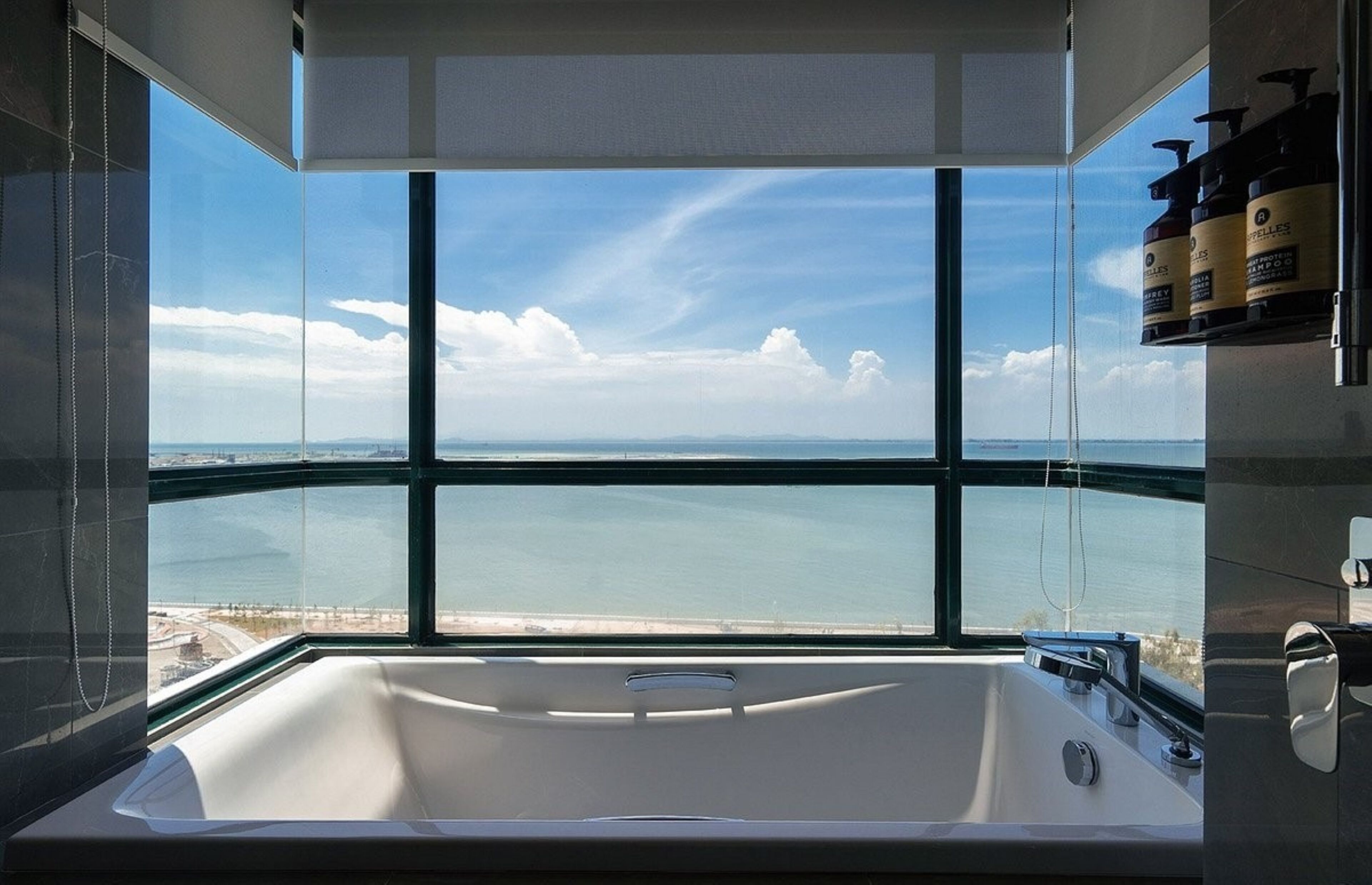 Um banheiro moderno com uma banheira grande, vista para o mar e área de chuveiro.