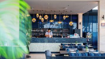 Un espace bar moderne avec un barman, des sièges dotés de coussins bleus et une variété de bouteilles exposées sur des étagères.