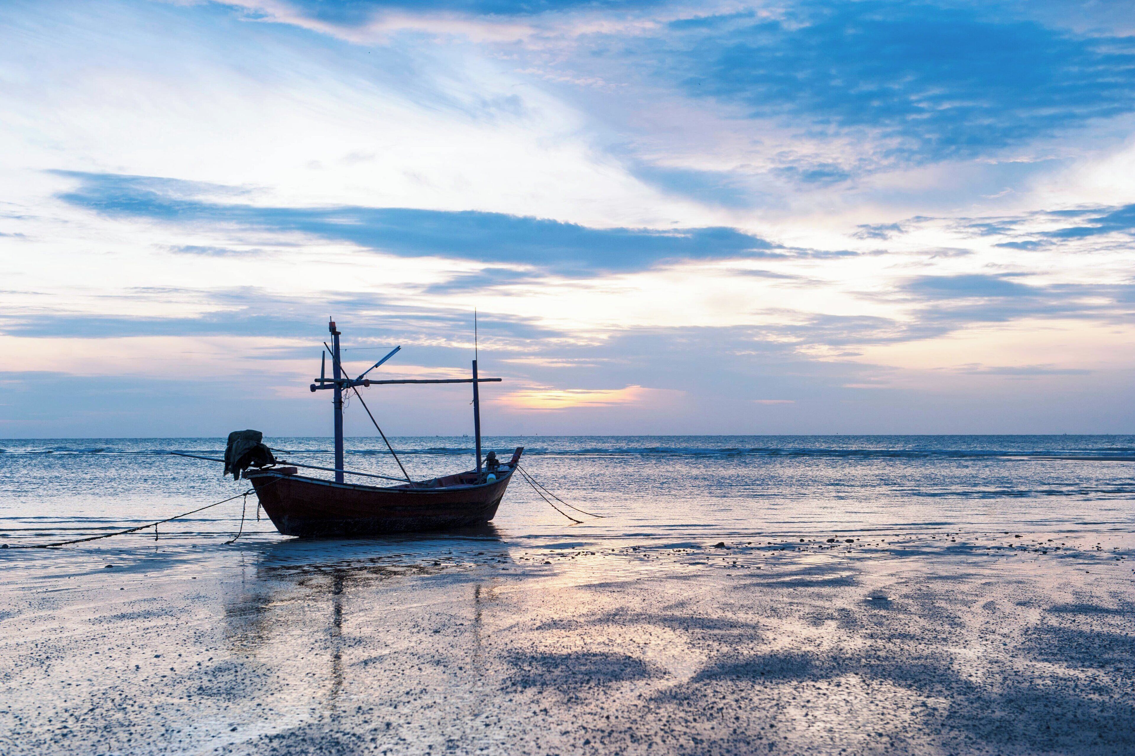 A boat on a beach with a calm sea and a clear sky.