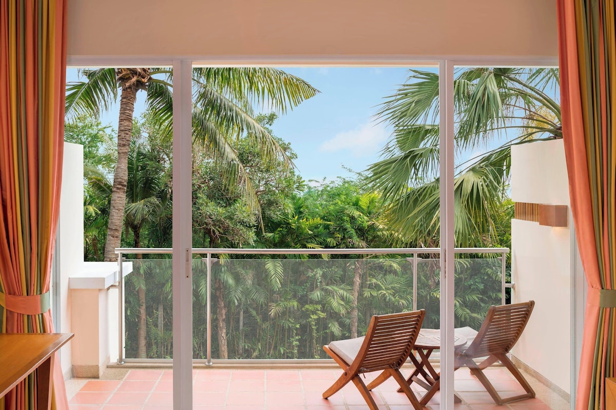 A balcony with a glass door, two wooden chairs, and a table.