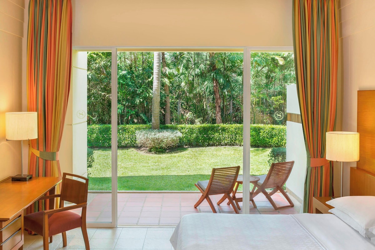 A hotel room with a large window, a bed, a desk, and two chairs.