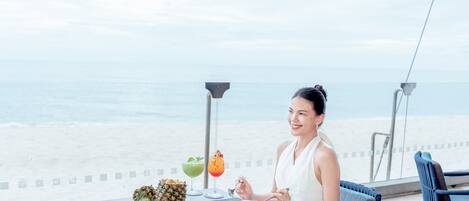 A dining table with various dishes and drinks, overlooking a beach.