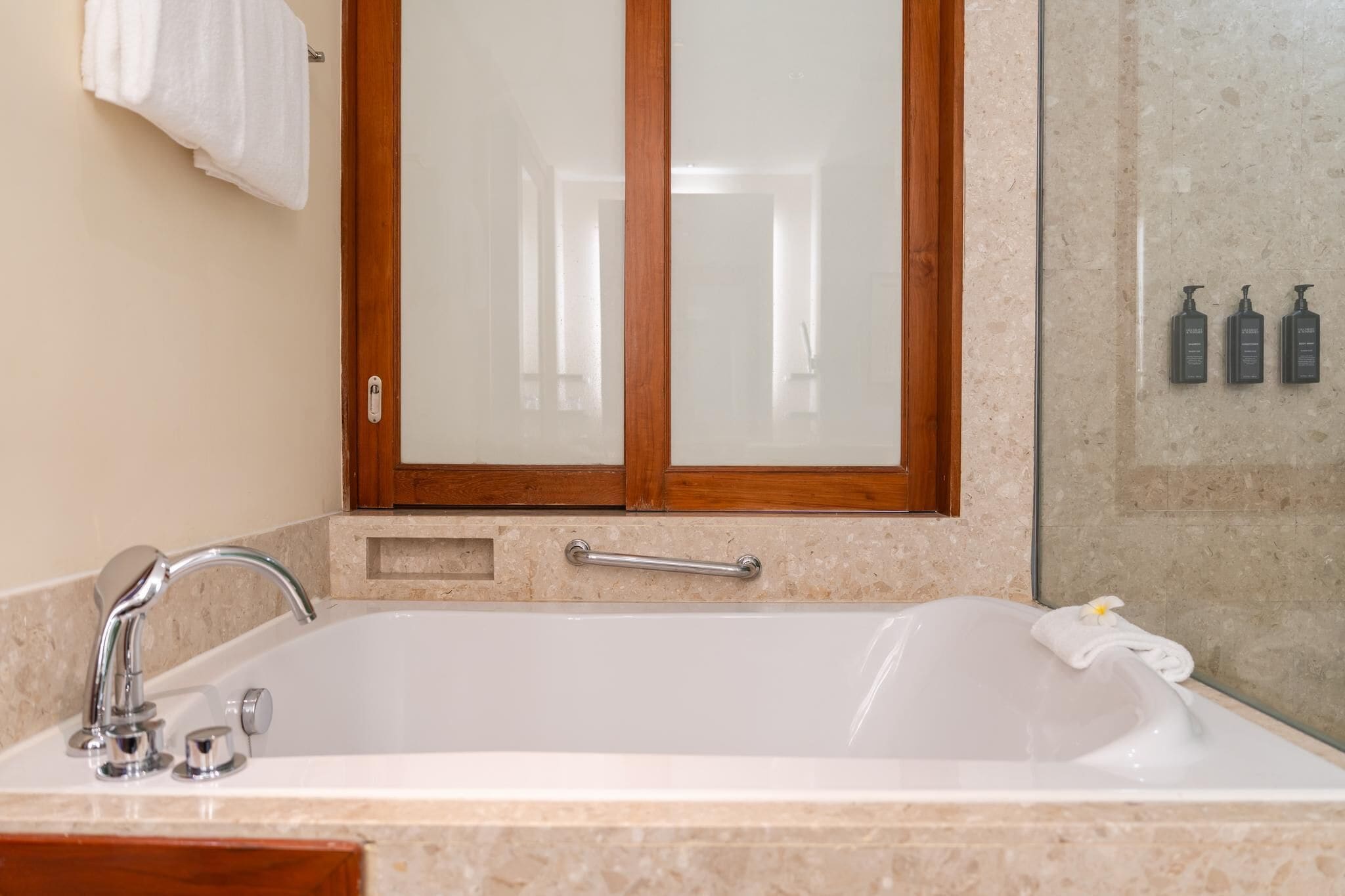 Une salle de bain avec une baignoire blanche, une fenêtre à cadre en bois, un porte-serviettes et une cabine de douche en verre.