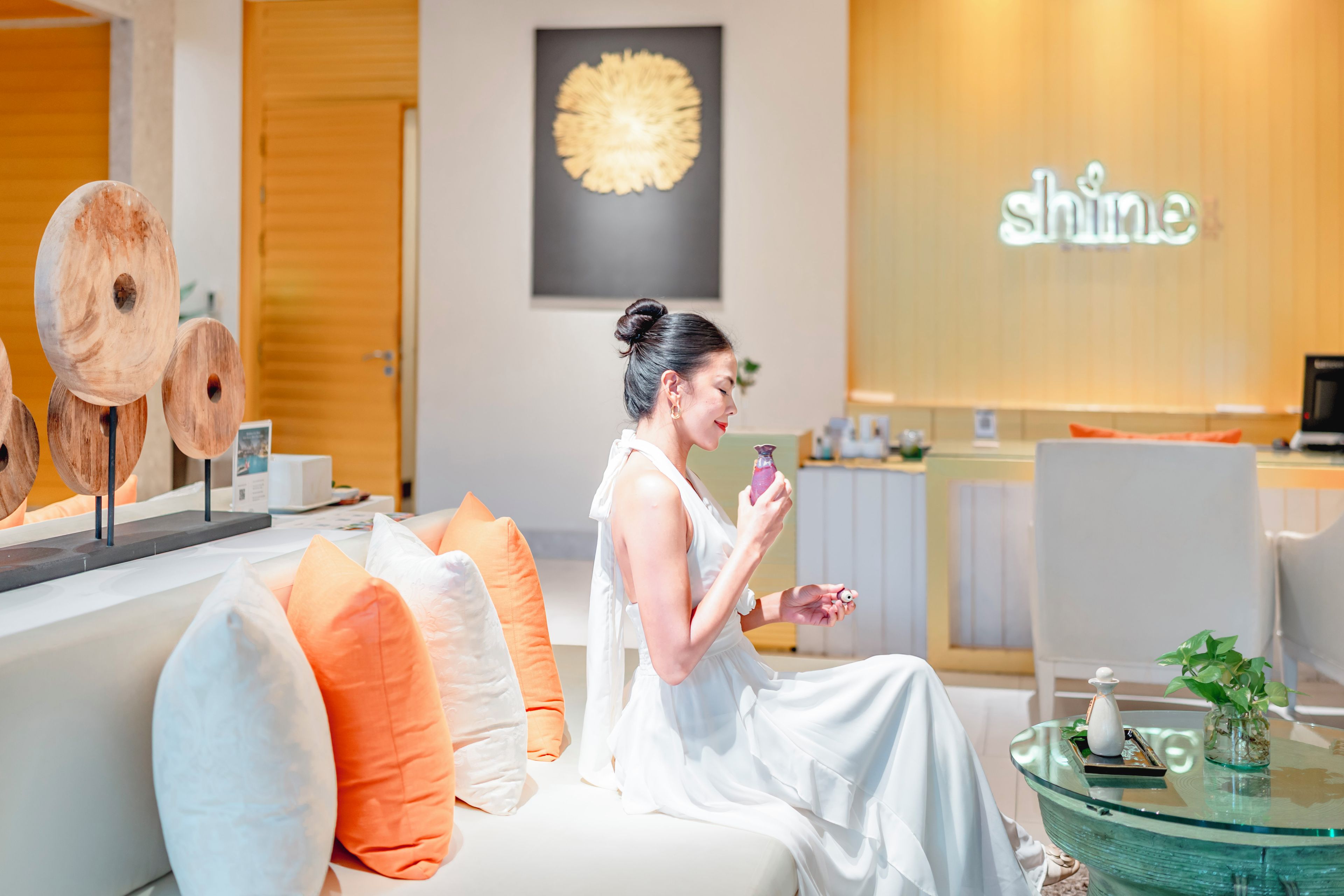 Une femme est assise sur un canapé, devant une table en verre, et tient un téléphone à la main.